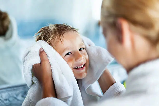 Mother drying up child's hair with a towel in a bathroom after bath.