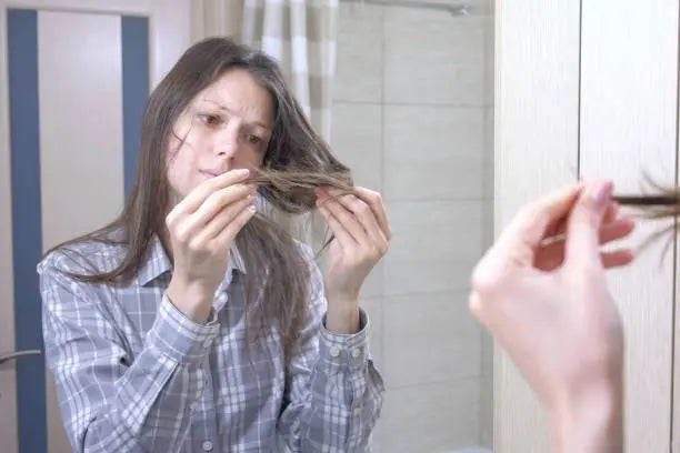 Woman looks at her dry, brittle hair in the bathroom