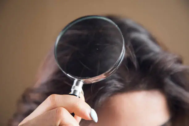 young woman looking at her hair with a magnifying glass